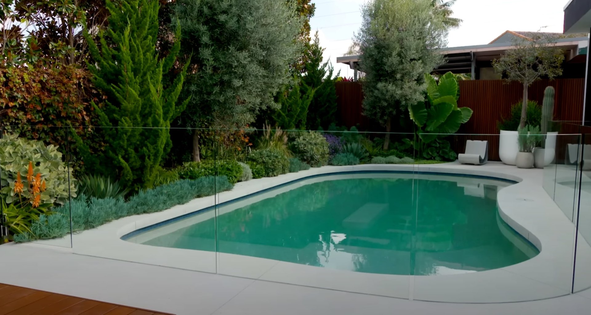 Contemporary pool landscape design with glass safety fencing and lush tropical plants Modern swimming pool with glass fencing and tropical landscaping in Channelview, TX